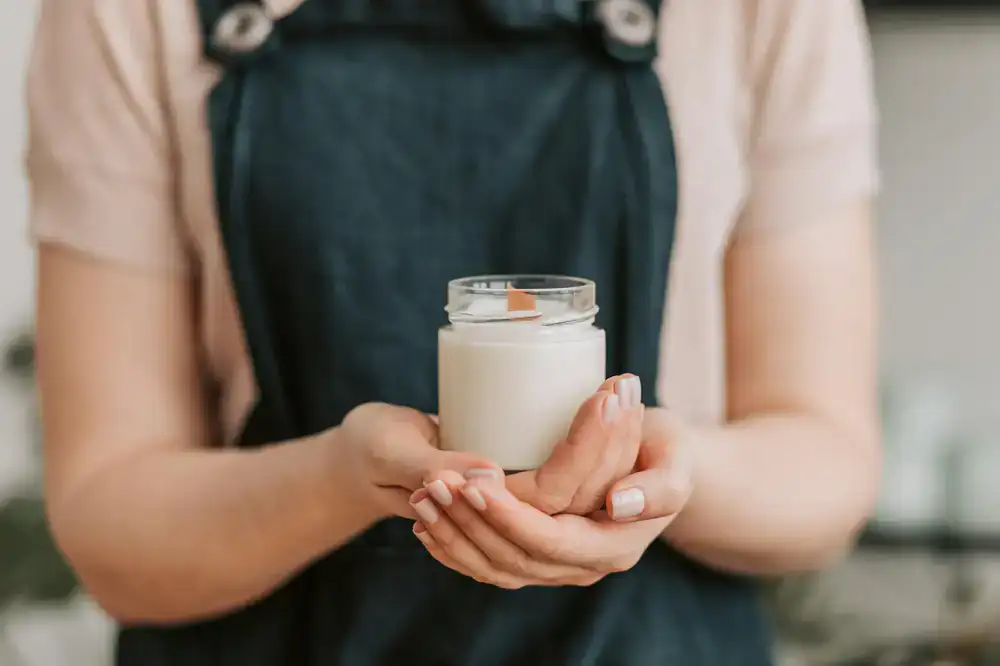 Hands carefully placing a cotton wick into a glass jar